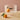 Clear ribbed glass pedestal trifle bowl with a short cylindrical base containing an orange, photographed on a beige tabletop.