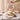 A hand lifting a clear glass cake dome to reveal a floral decorated cake. The table is also set with plates, bowls and teacups on a white tablecloth.