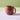 A matte terracotta coloured ceramic mug with a braided handle, shown on a multi coloured background.