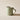 A classic ceramic mug with a sage green exterior and a soft cream interior with a curved handle. Photographed on a beige coloured background with strong shadows.