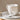 A white stoneware mug with a vertical ribbed texture and a curved handle, shown resting on two matching plates with a stainless steel teaspoon.