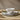 A single setting of a white stoneware dinnerware set with a textured radial ribbed pattern, including a dinner plate, side plate, and bowl, shown stacked on a cream placemat upon a wooden tabletop. A knife lies across the smaller plate.