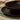 A black stoneware bowl with a radiating ribbed texture, stacked on a matching dinner plate that is resting on a green woven placemat upon a wooden table top.