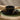 A single setting of a black stoneware dinnerware set with a textured radial ribbed pattern, including a dinner plate, side plate, and bowl, shown stacked on a green placemat on a wooden table top. A knife and piece of toast lay upon the smaller plate.
