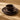 A single setting of a dark brown stoneware dinnerware set with a textured radial ribbed pattern, including a dinner plate, side plate, and bowl, shown stacked on a wooden tabletop.